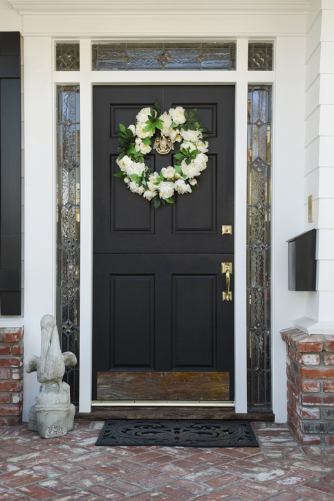 Exterior view of a front door to a residence with brick flooring and a wreath on the door. Vertical shot.